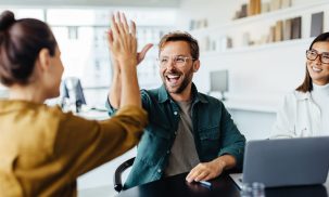 Two team members high-five each other while another looks on. They appear to have plenty of energy and enthusiasm.