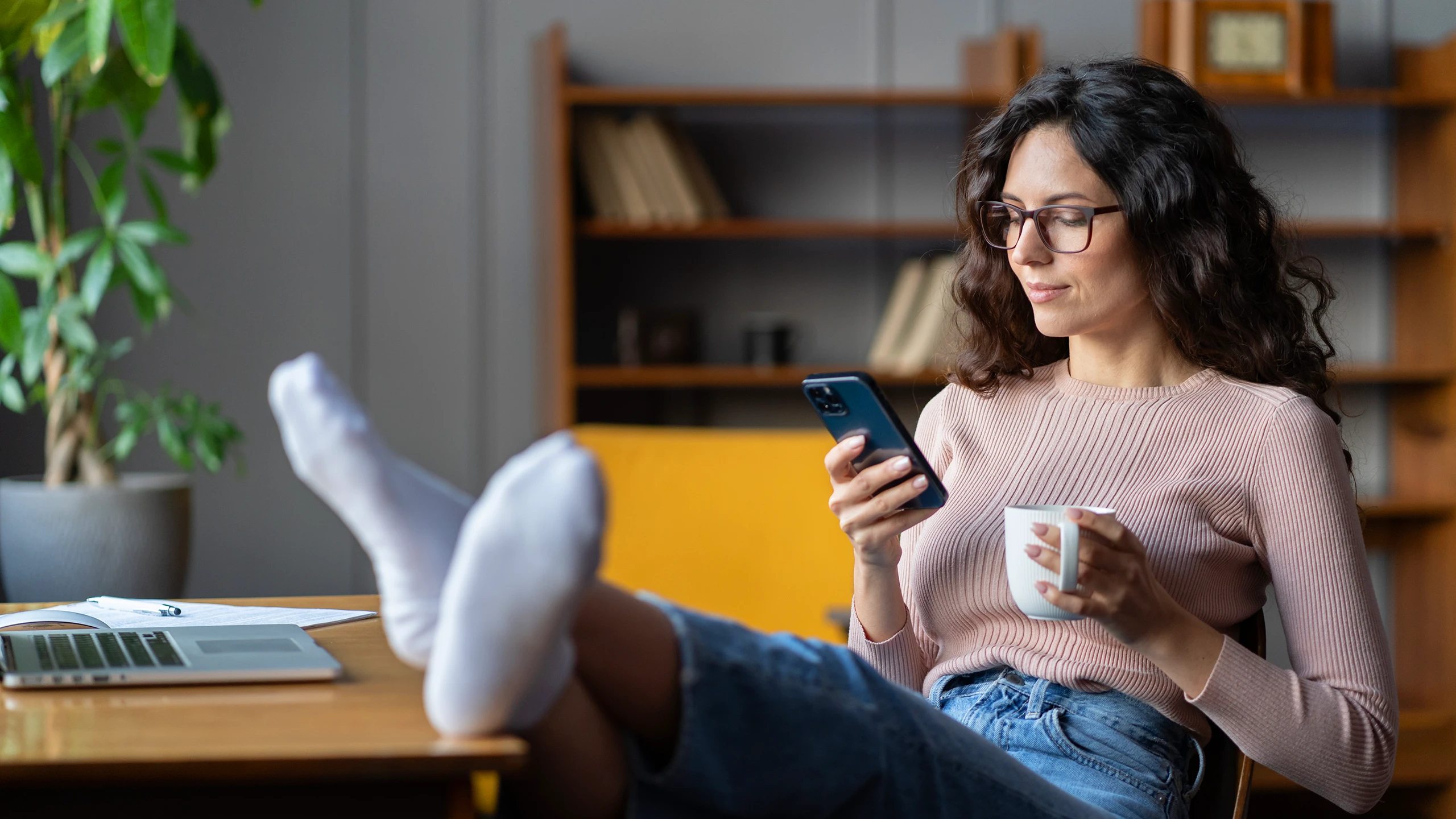 A woman procrastinates at work by looking at her phone and sipping coffee. Who among us, am I right?